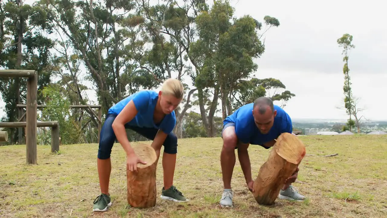 Fit man and woman lifting heavy wooden logs during obstacle course