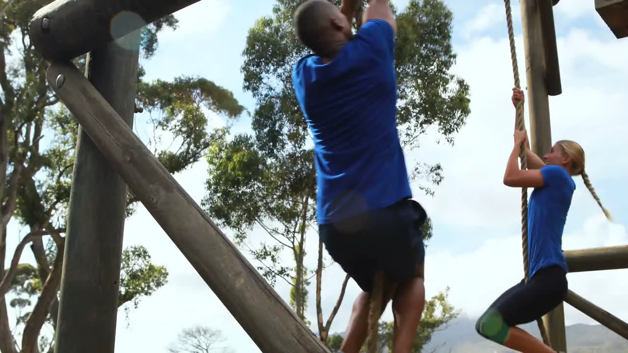 Fit man and woman climbing rope during obstacle course