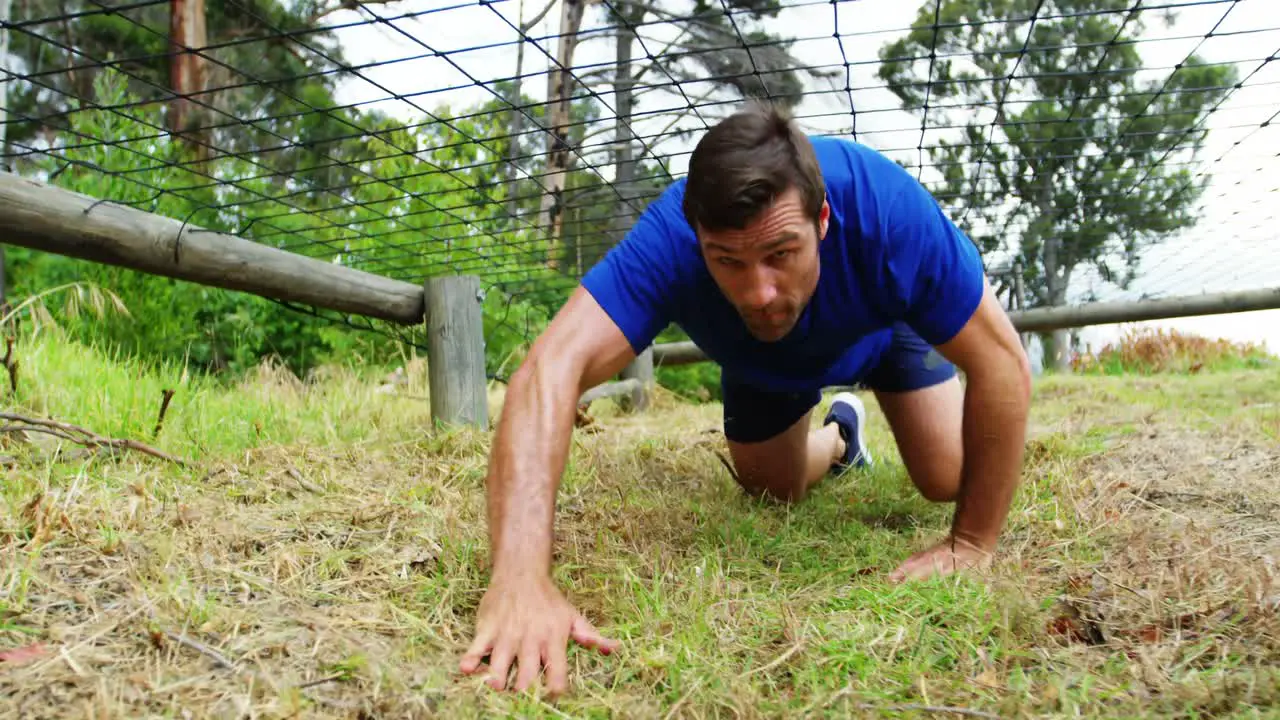 Fit man crawling under the net during obstacle course 4k