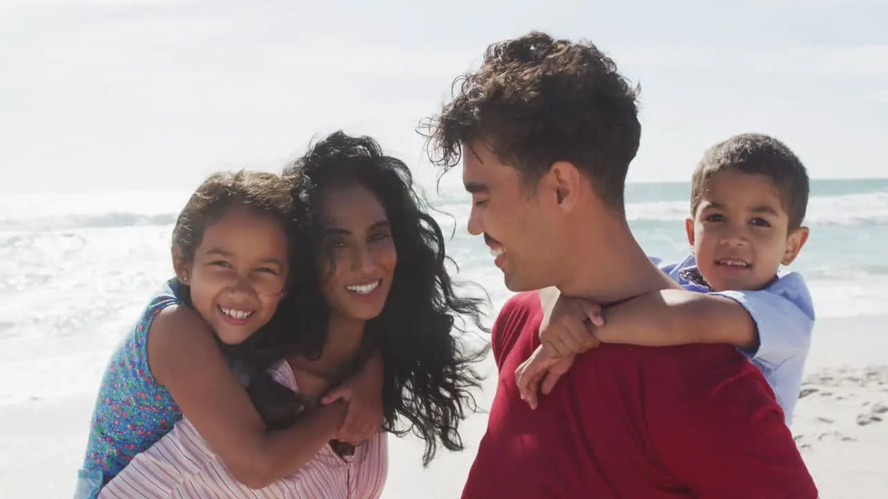 Portrait of happy hispanic parents carrying children on piggyback on beach