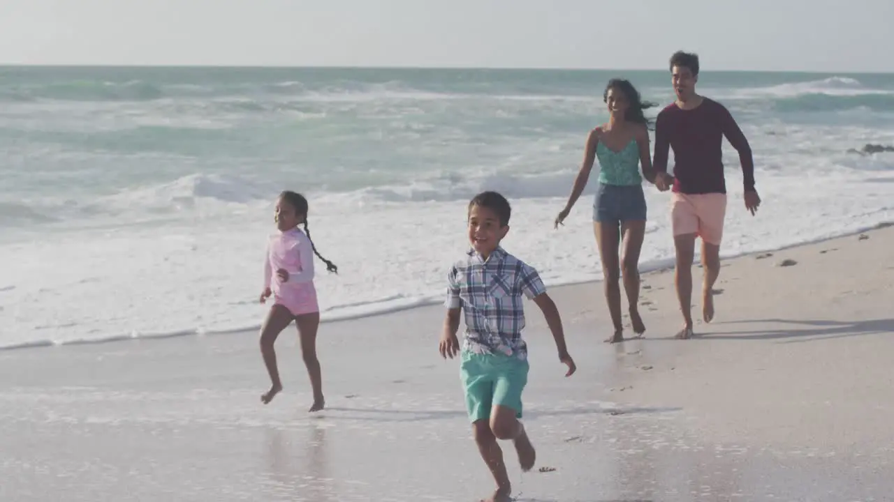 Happy hispanic mother father son and daughter running on beach