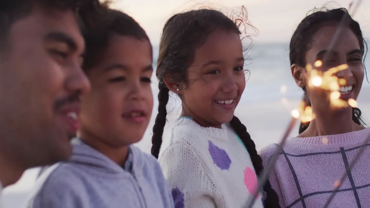 Portrait of happy hispanic family playing with sparklers on beach at sunset