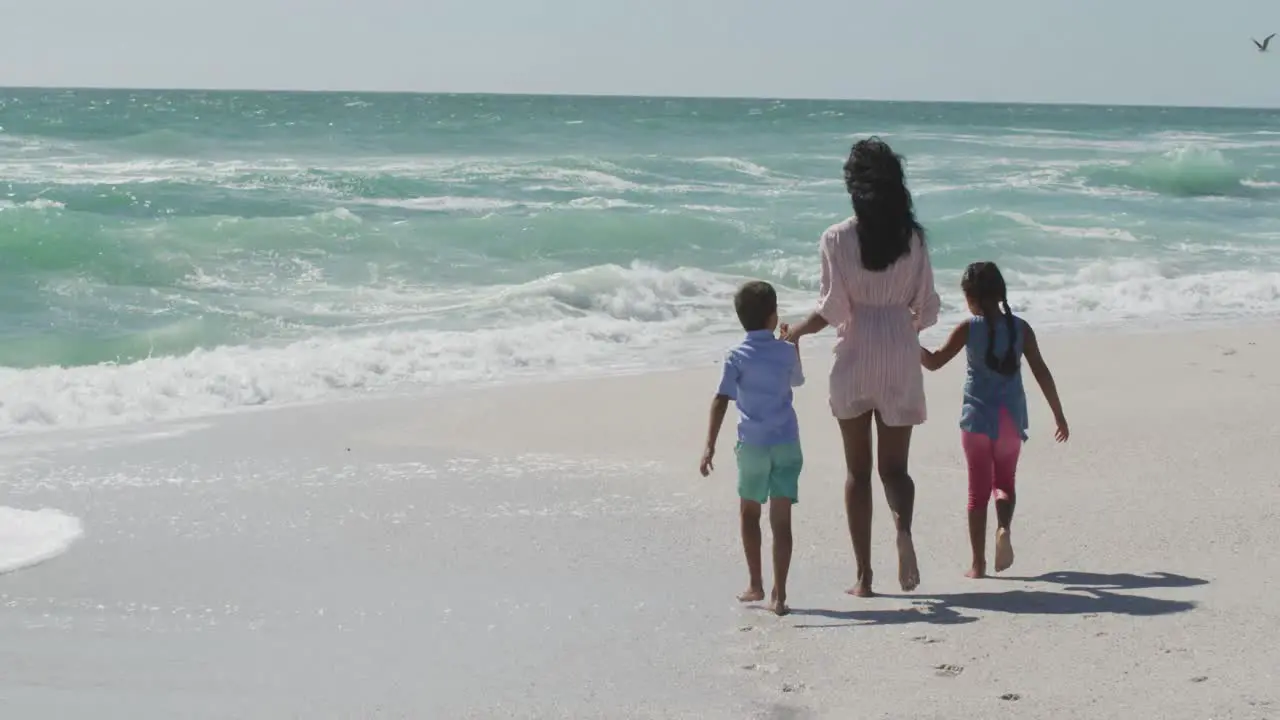 Back view of hispanic mother with daughter and son walking on beach