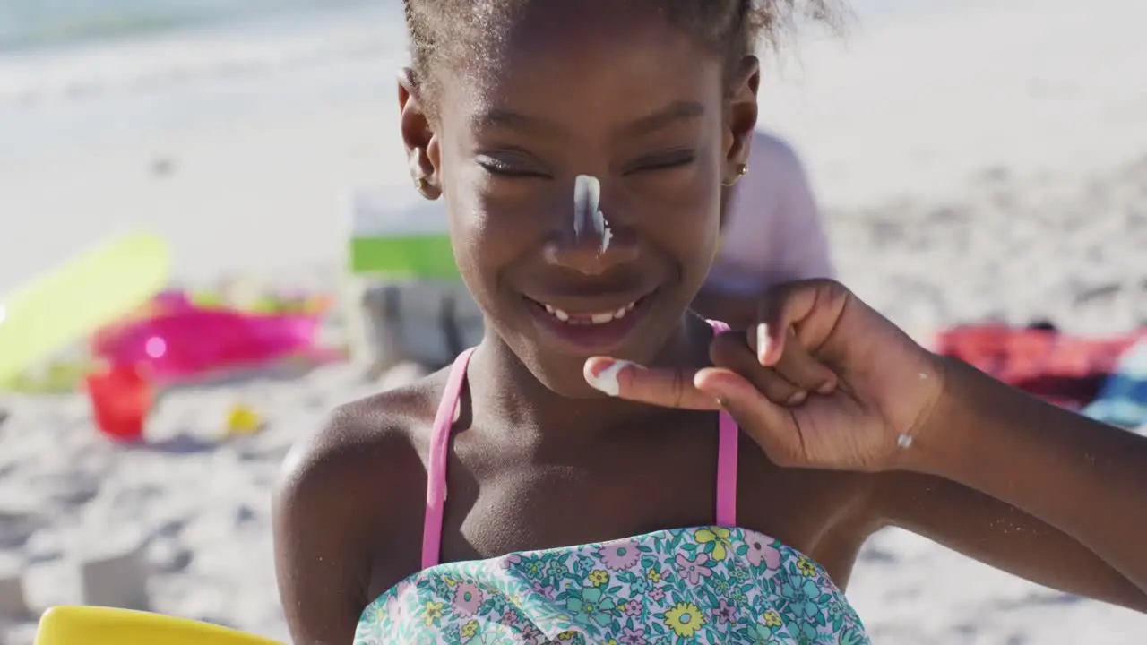 Video of happy african american daughter with sunscreen on beach