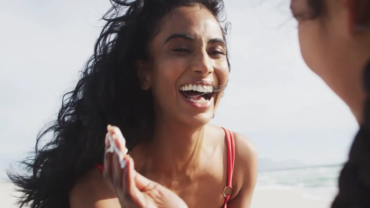 Happy hispanic mother applying sun cream on daughter face on beach