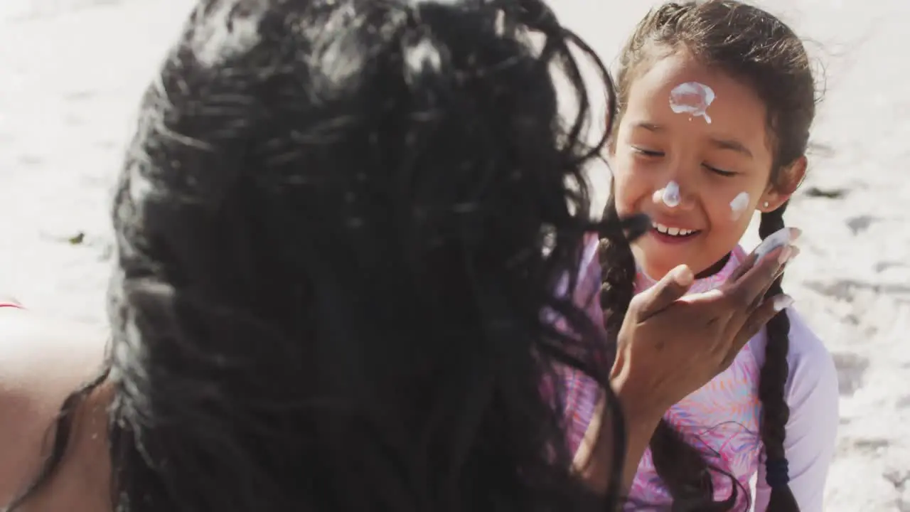 Hispanic mother applying sun cream on happy daughter face on beach