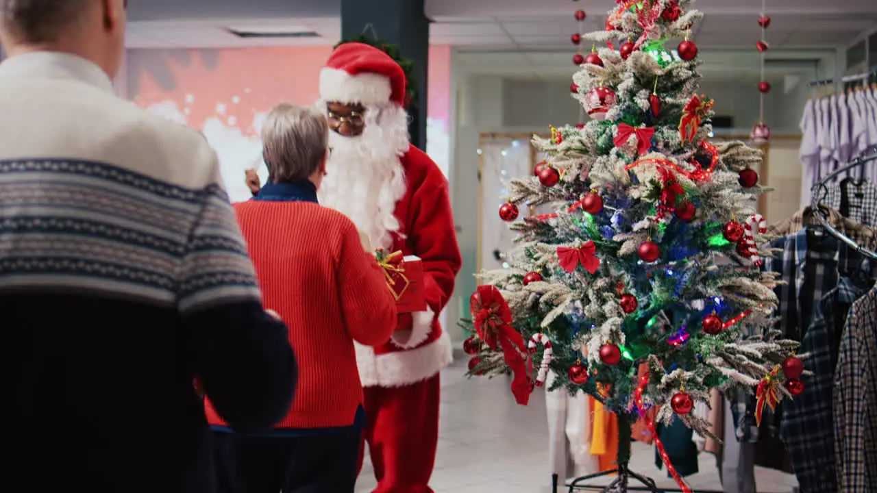 Employee wearing Santa Claus suit holding raffle contest in Christmas decorated shopping mall clothing shop during winter holiday season inviting elderly couple to participate