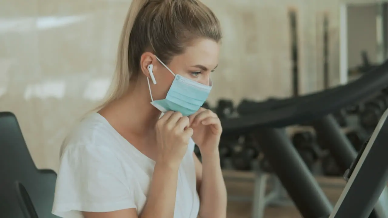 Young Sporty Woman Puts On Face Mask Ands Uses An Exercise Machine In The Gym