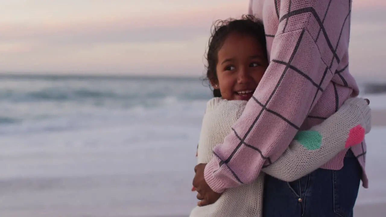 Midsection of hispanic mother embracing daughter on beach at sunset