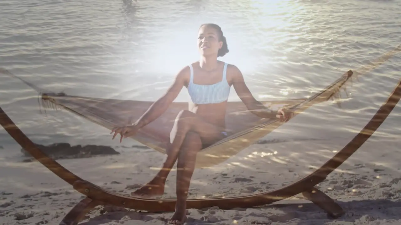 Animation of light over happy african american woman in hammock on beach