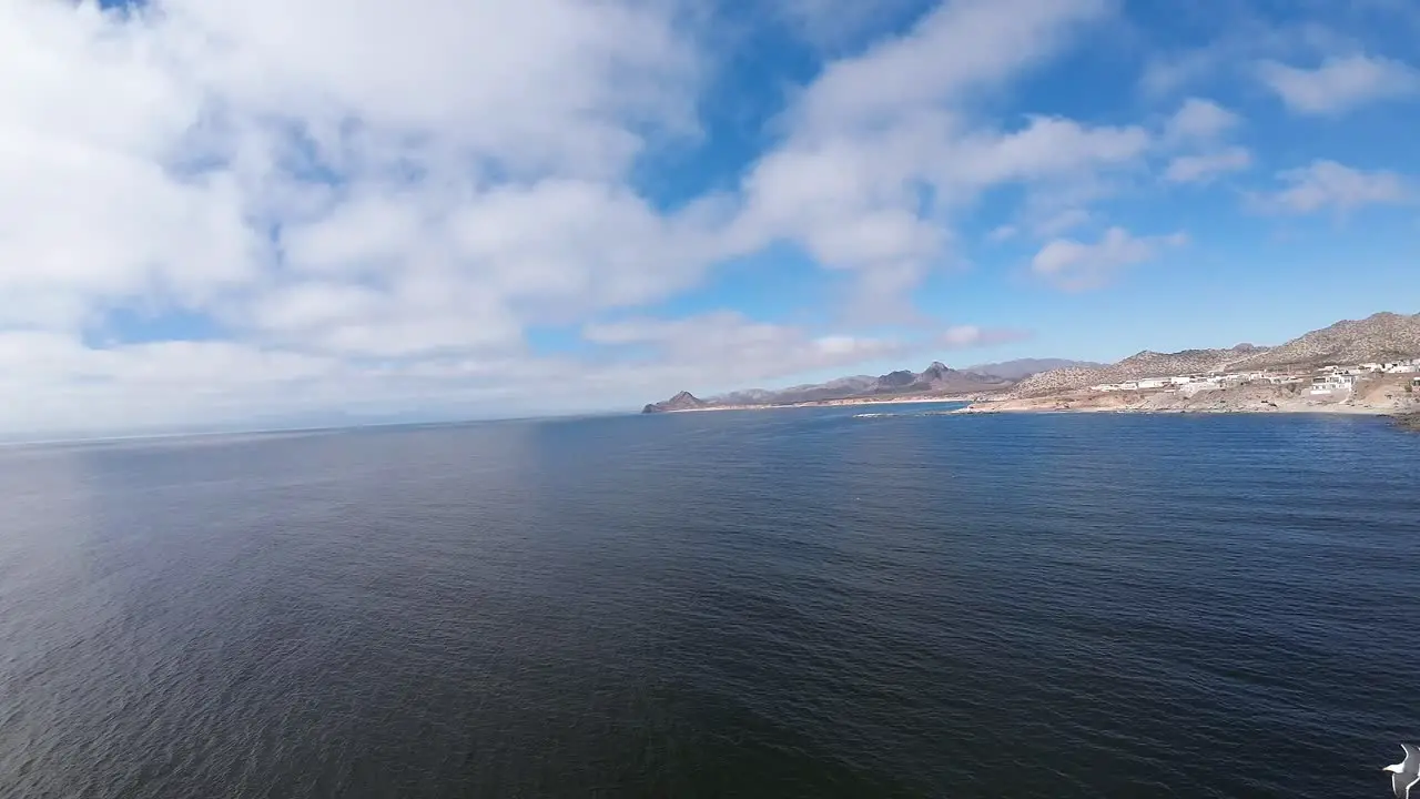 Drone flies above the sea in an open and high shot with a distant view of the coast with houses on the shore