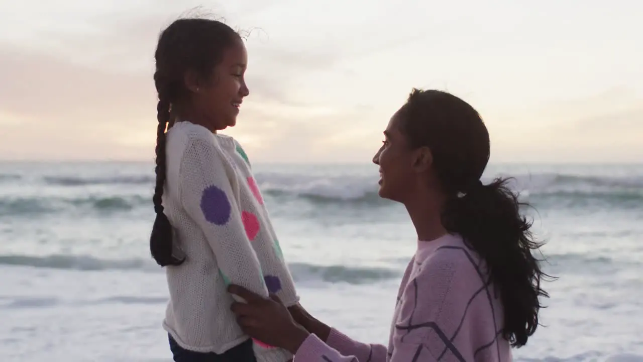 Happy hispanic mother and daughter on beach at sunset