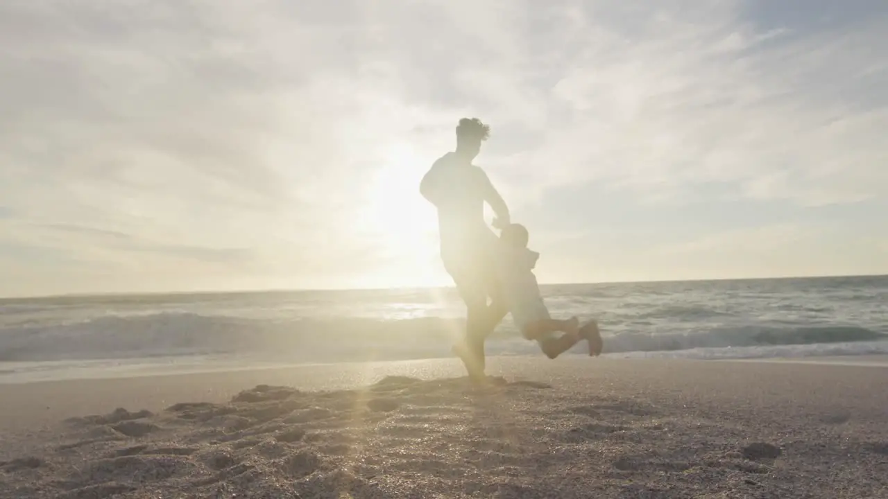 Hispanic father playing with son on beach at sunset