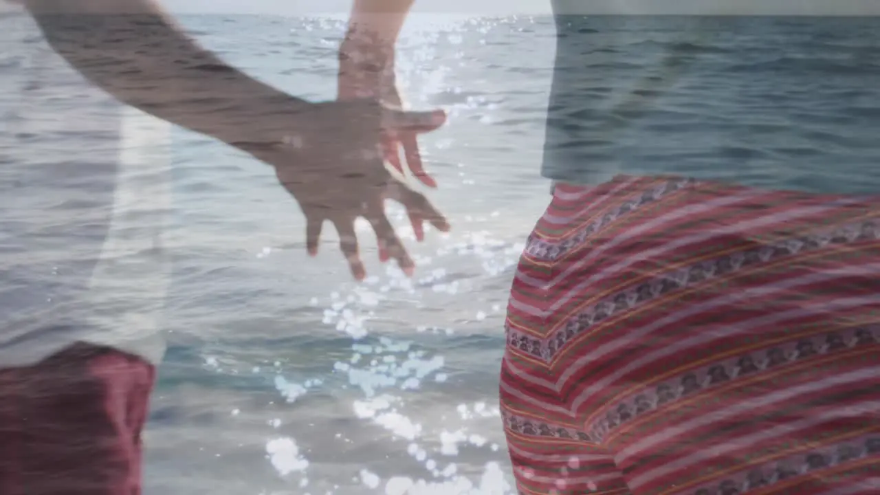 Animation of lights over hands of african american couple walking on beach