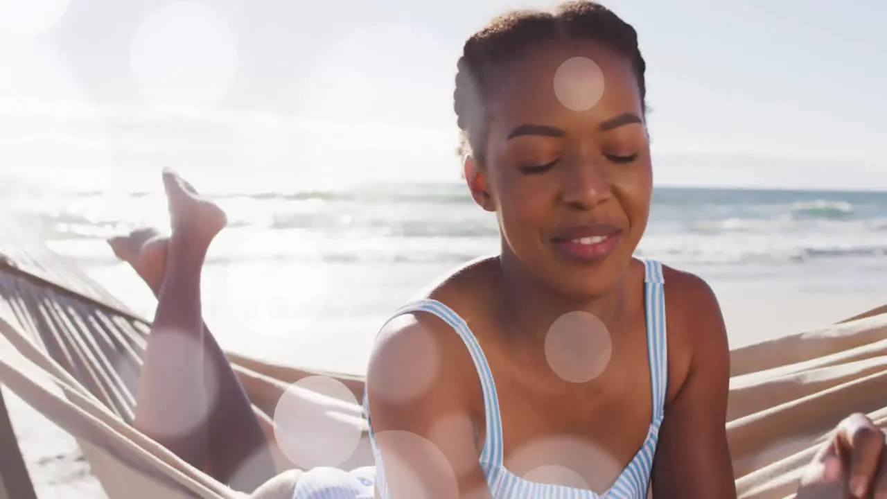 Animation of dots over happy african american woman in hammock on beach