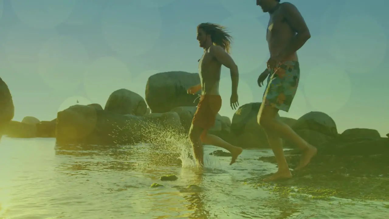 Animation of glowing lights over group of male friends running to the sea