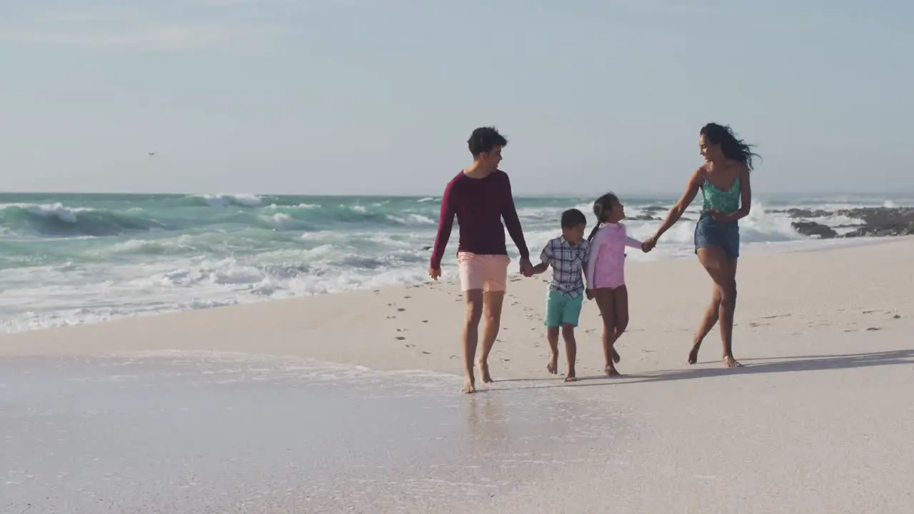 Happy hispanic mother father son and daughter holding hands and walking on beach