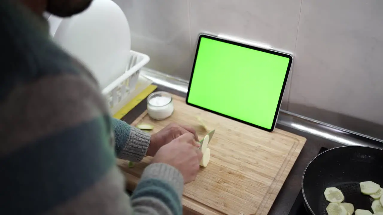 Over the shoulder shot of a man cutting zucchini while following a recipe from his tablet