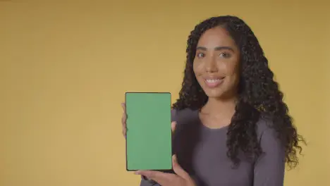 Studio Portrait Of Smiling Woman Holding Up Digital Tablet With Green Screen