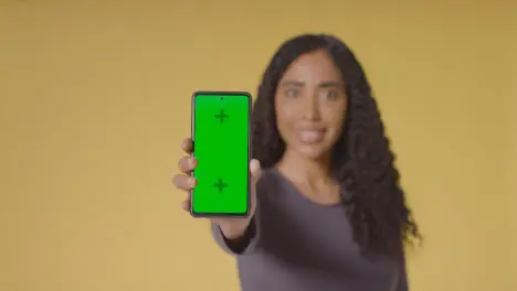 Studio Portrait Of Smiling Woman Holding Up Mobile Phone With Green Screen