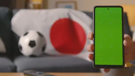 Green Screen Mobile Phone With Japanese Flag Draped Over Sofa At Home Ready For Soccer Match