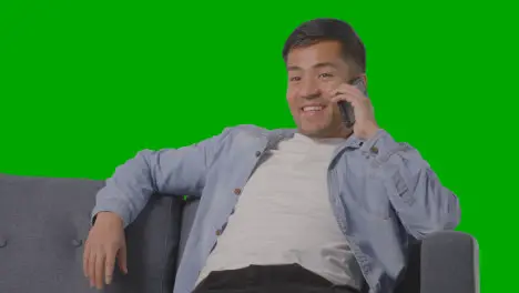 Studio Shot Of Young Man Sitting On Sofa Talking On Mobile Phone Against Green Screen 1