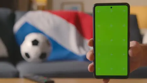 Green Screen Mobile Phone With Dutch Flag Draped Over Sofa At Home Ready For Soccer Match