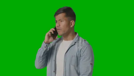 Studio Shot Of Angry Casually Dressed Young Man Talking On Mobile Phone Against Green Screen 