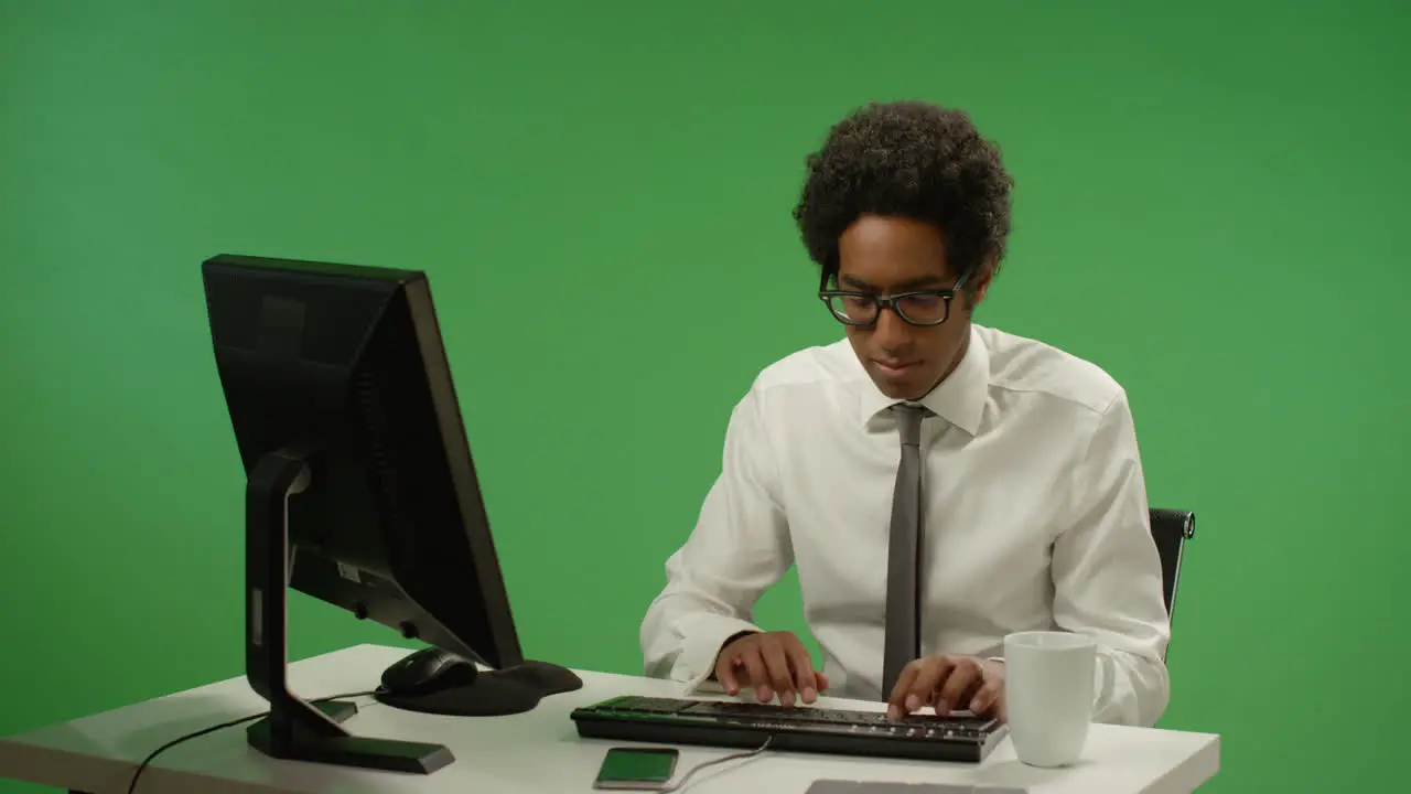 Businessman sitting at desk typing on green screen