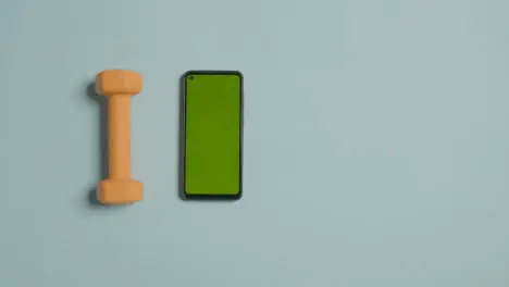 Overhead Fitness Studio Shot Of Male Hand Picking Up Exercise Dumbbell Weights Next To Green Screen Mobile Phone