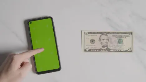 Overhead Currency Shot Of US 5 Dollar Bill Next To Person Using Green Screen Mobile Phone