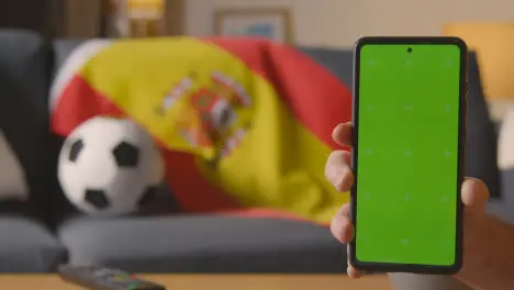 Green Screen Mobile Phone With Spanish Flag Draped Over Sofa At Home Ready For Soccer Match