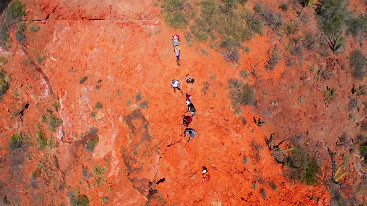 People rappelling on a red mountain by the sea