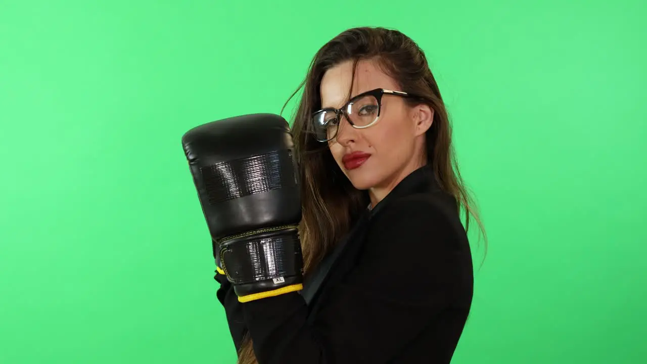 Sexy and seductive brunette young woman with glasses and business dress wear boxing gloves ready to fight daily life stress