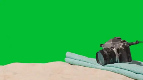 Summer Holiday Concept Of Person Picking Up Camera Beach Towel On Sand Against Green Screen