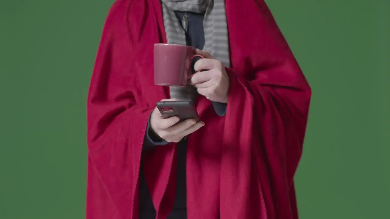 Close Up Of Person Wearing Blanket With Hot Drink Using Mobile Phone Trying To Keep Warm In Energy Crisis 5