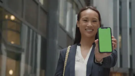 Portrait Of Businesswoman Outside City Of London Offices Holding Up Green Screen Mobile Phone