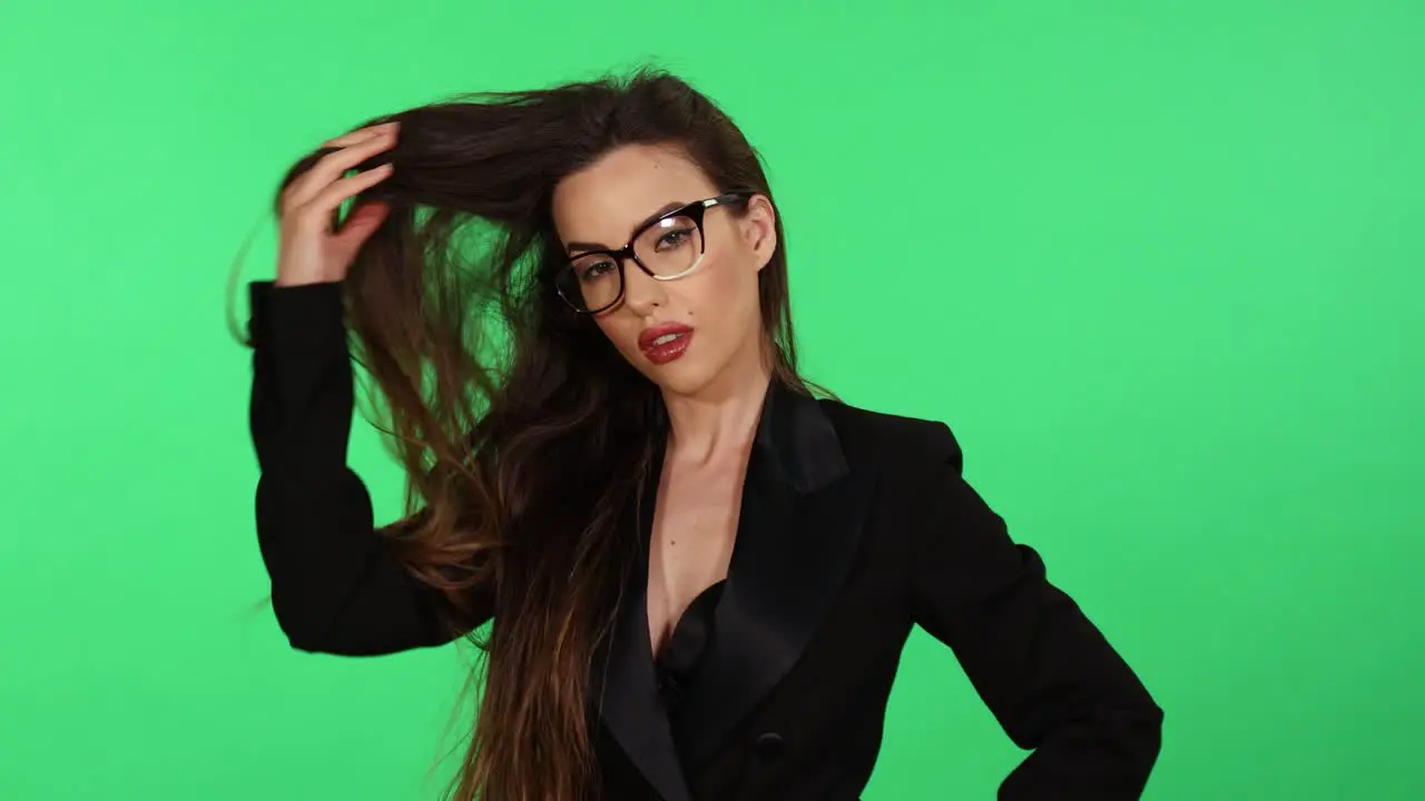 Sexy long hair brunette young woman in formal black business office suit and glasses touches hair while looking at camera