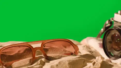 Summer Holiday Concept Of Sunglasses Camera Beach Towel On Sand Against Green Screen