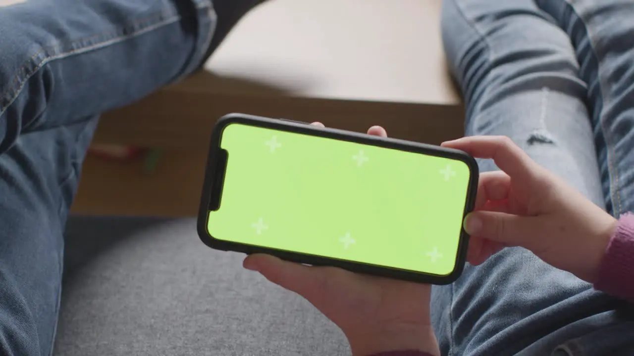 Close Up Of Two Children Sitting On Sofa At Home Looking At Green Screen Mobile Phone 1