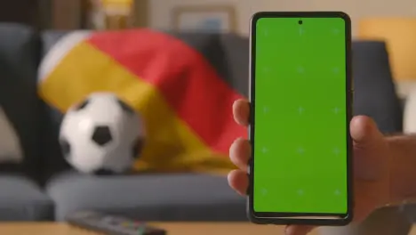 Green Screen Mobile Phone With German Flag Draped Over Sofa At Home Ready For Soccer Match