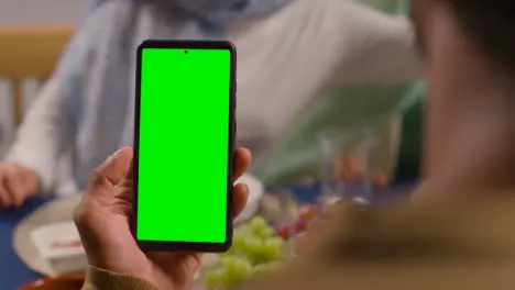 Man Looking At Green Screen Mobile Phone Sitting Around Muslim Muslim Family Table At Home Eating Meal