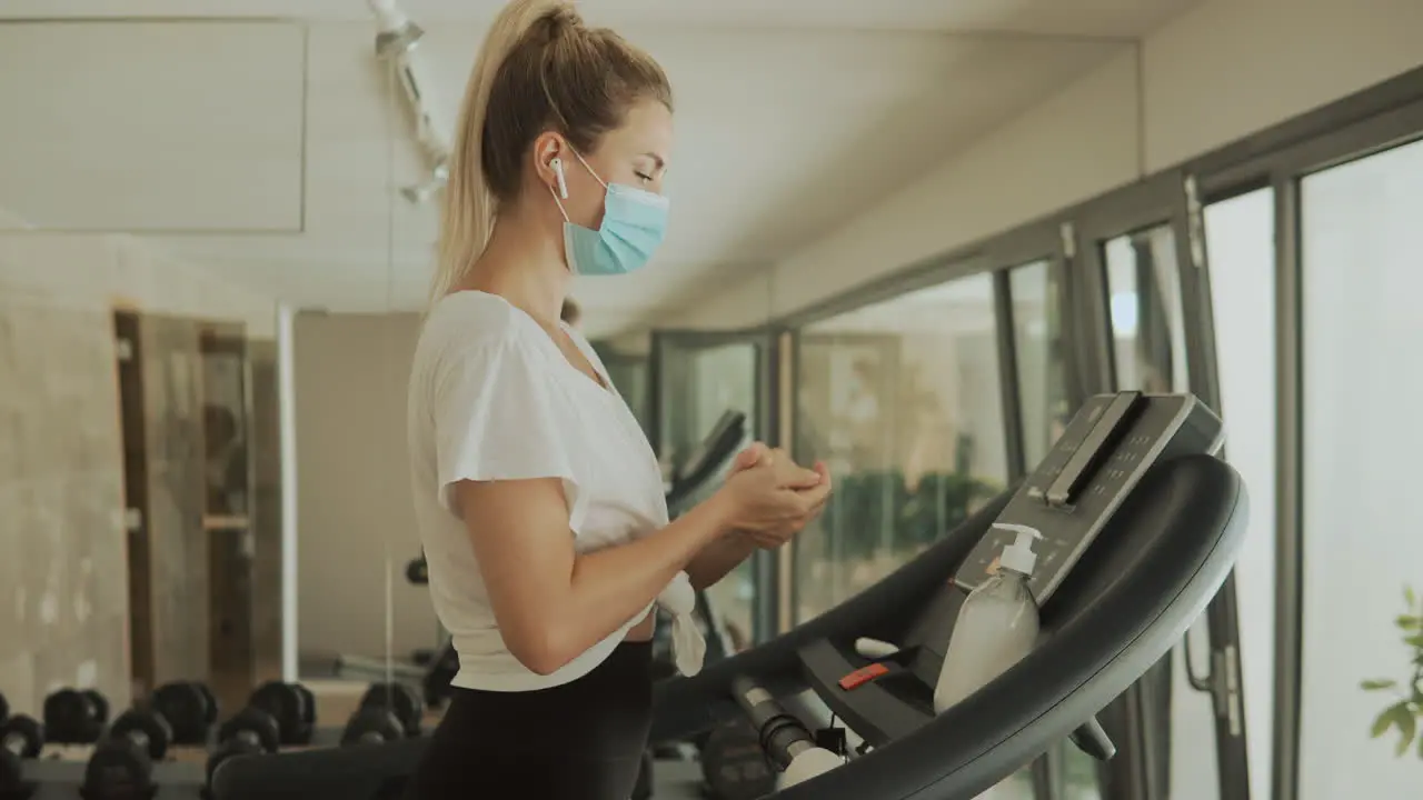 Young Athlete Female With Face Mask Uses An Exercise Machine And Hand Sanitizer In The Gym