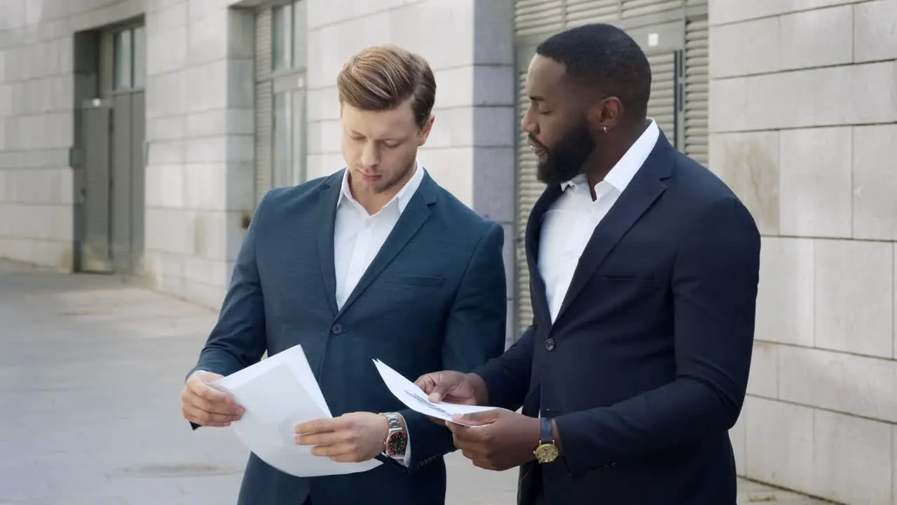 Businessmen discussing documents on streetEmployees standing on street together