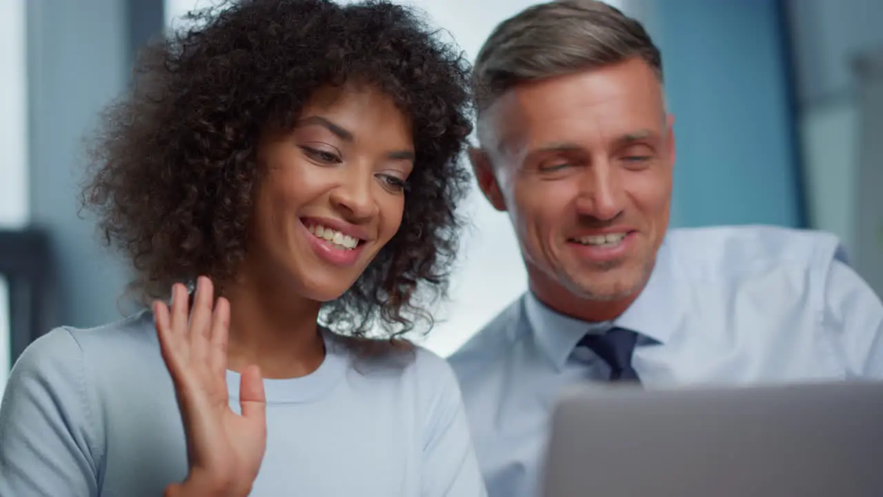 Businessman and businesswoman waving hands hi at camera during online video call