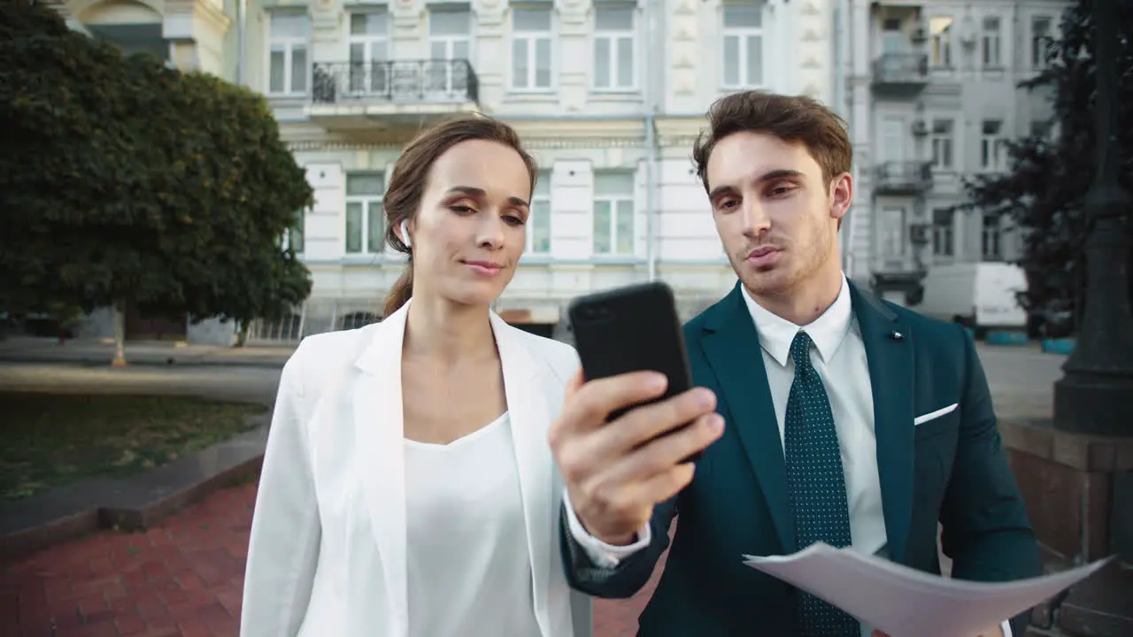 Friendly business man showing smiling woman information on phone on city walk