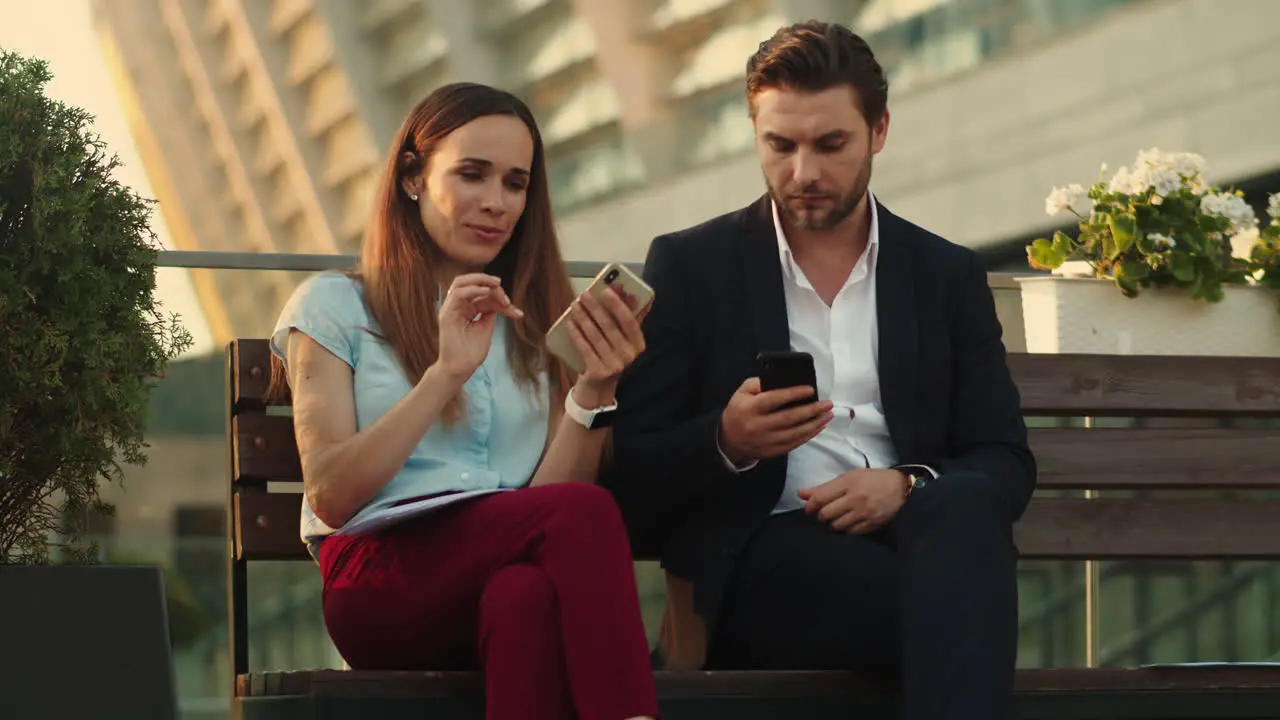 Confident businessman and businesswoman using smartphones in modern city