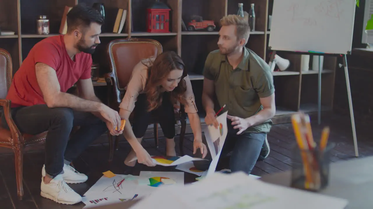 Joyful startup team discussing business plan documents at floor in office