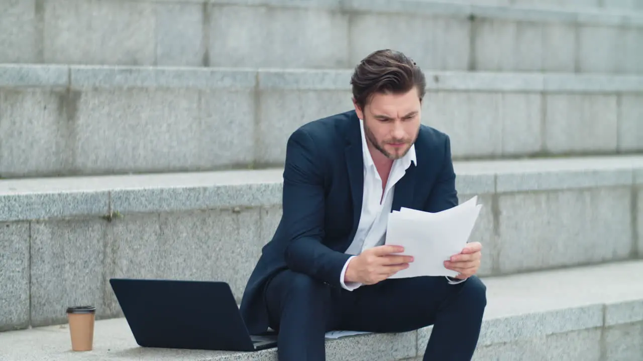 Businessman reading business papers on street Worried man sitting on stairs