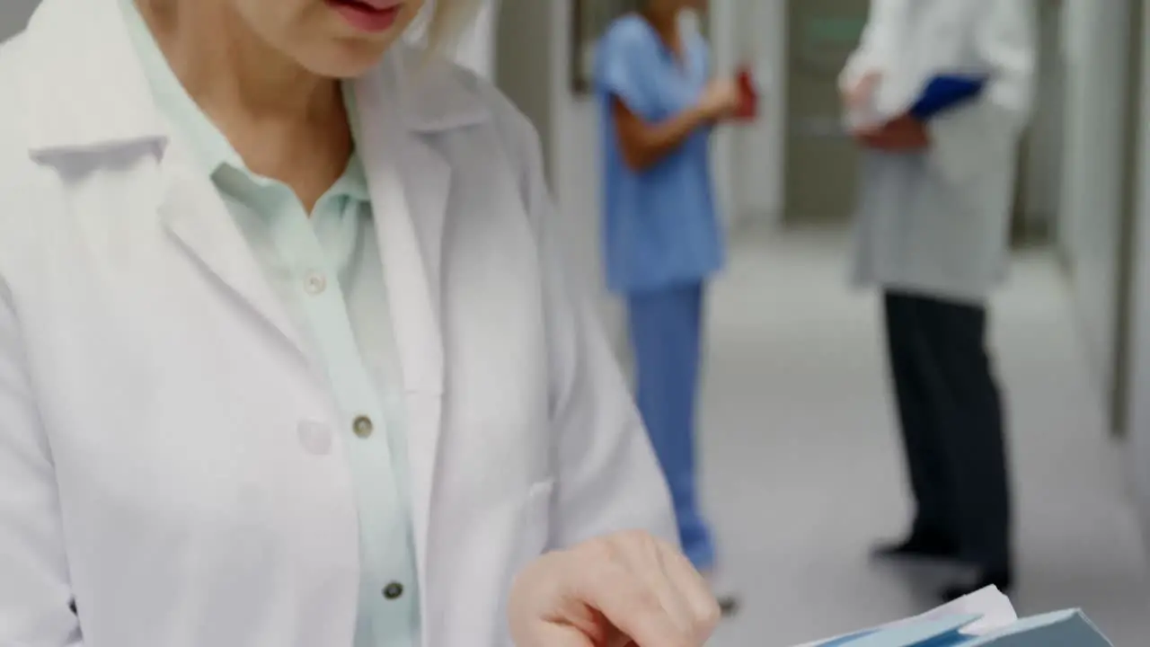 Female surgeon checking medical reports while colleague discussing in background